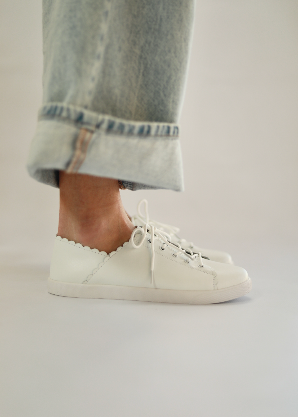 White sneakers worn with rolled-up jeans on a plain background