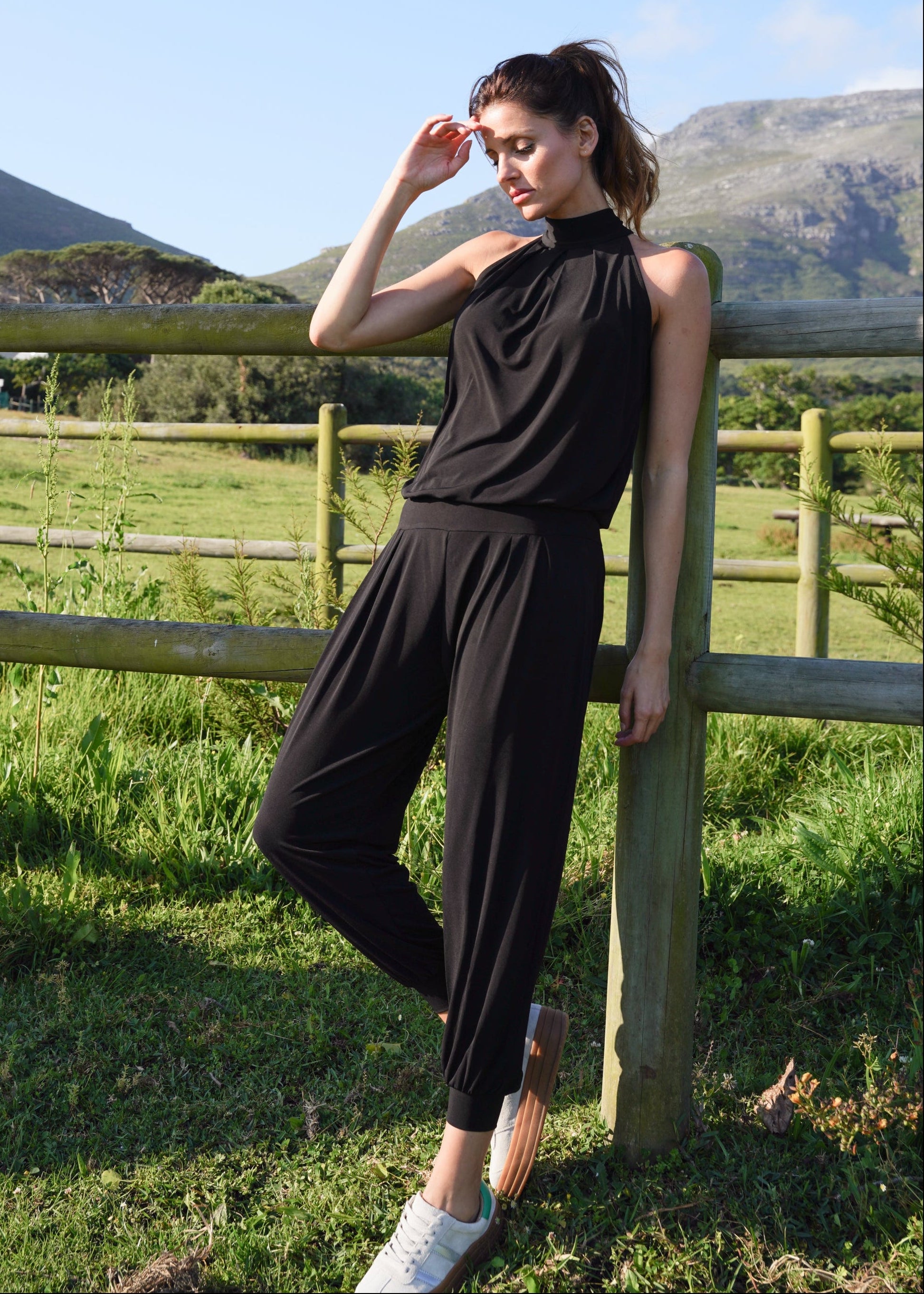 Woman in black outfit standing by a wooden fence with mountains in the background