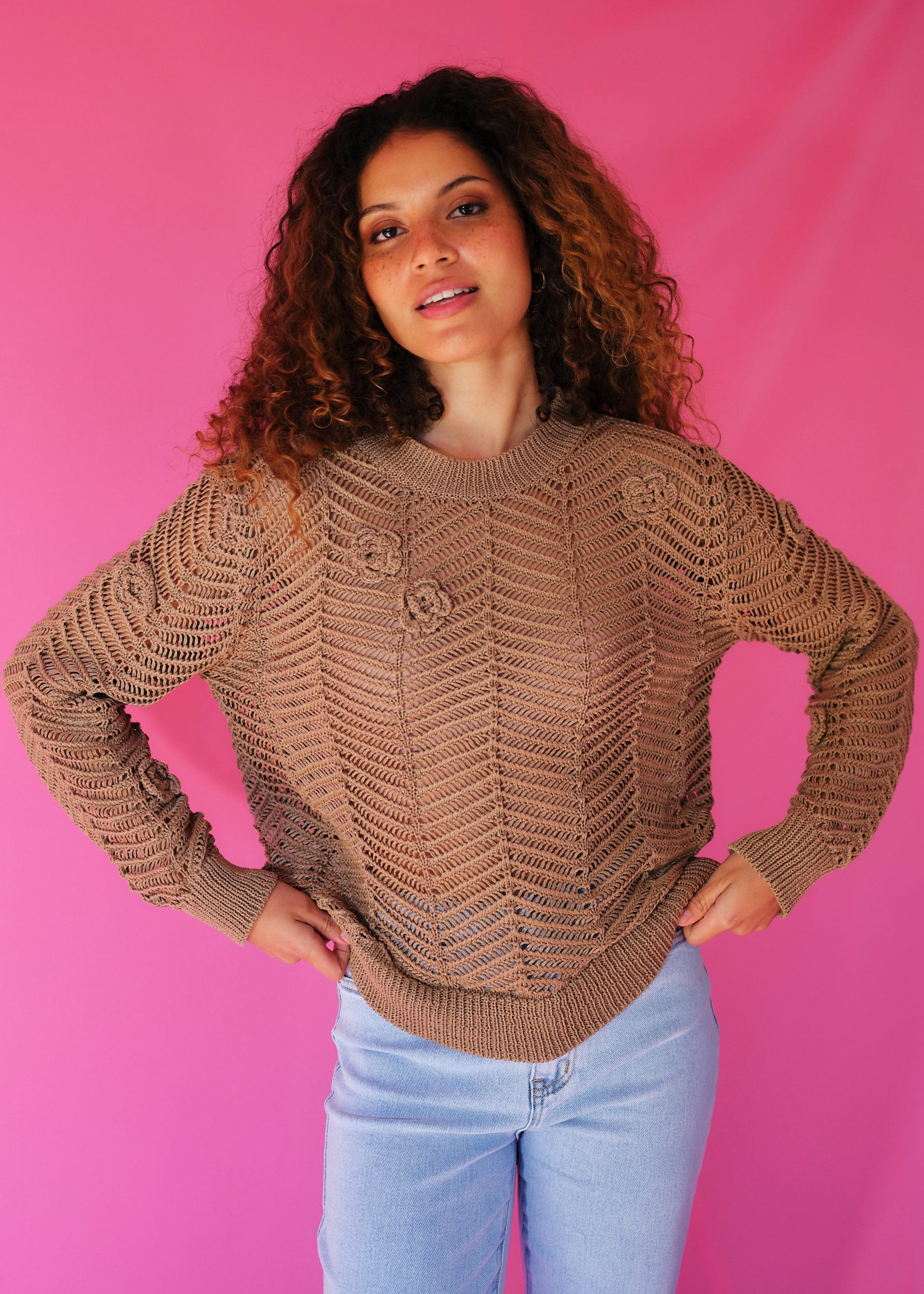 Woman wearing a brown knitted sweater against a pink background